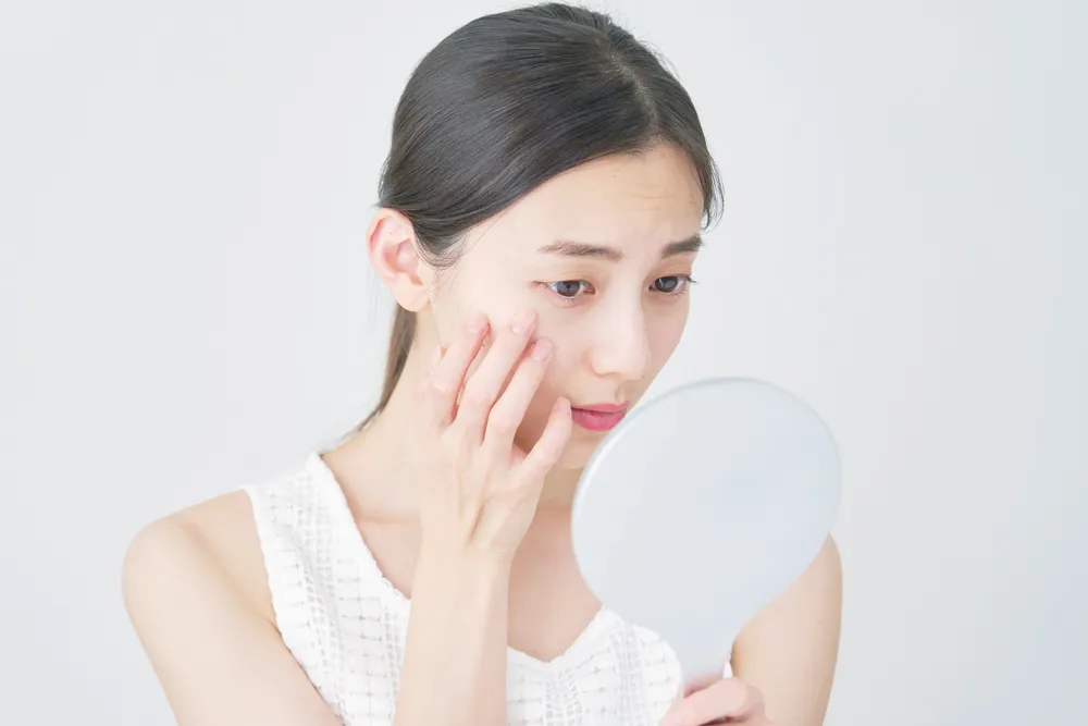 鏡で肌の状態をチェックする女性。ニキビやしこり、肌荒れなど、新宿本院では保険診療から美容皮膚科まで幅広く対応しています。
