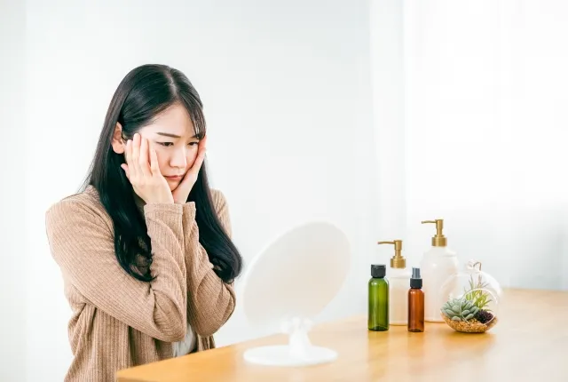鏡を見ながら顔の赤みや肌荒れ、酒さの症状に悩む女性のイメージ